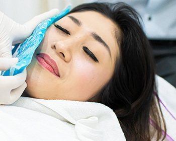 woman holding a cold compress to her face after getting dental implants in Lincoln